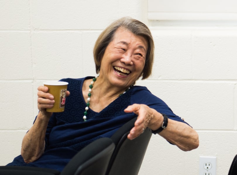 A woman laughs and gestures while holding a paper cup.