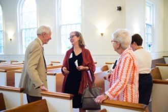 a small group of people talk and laugh standing between church pews